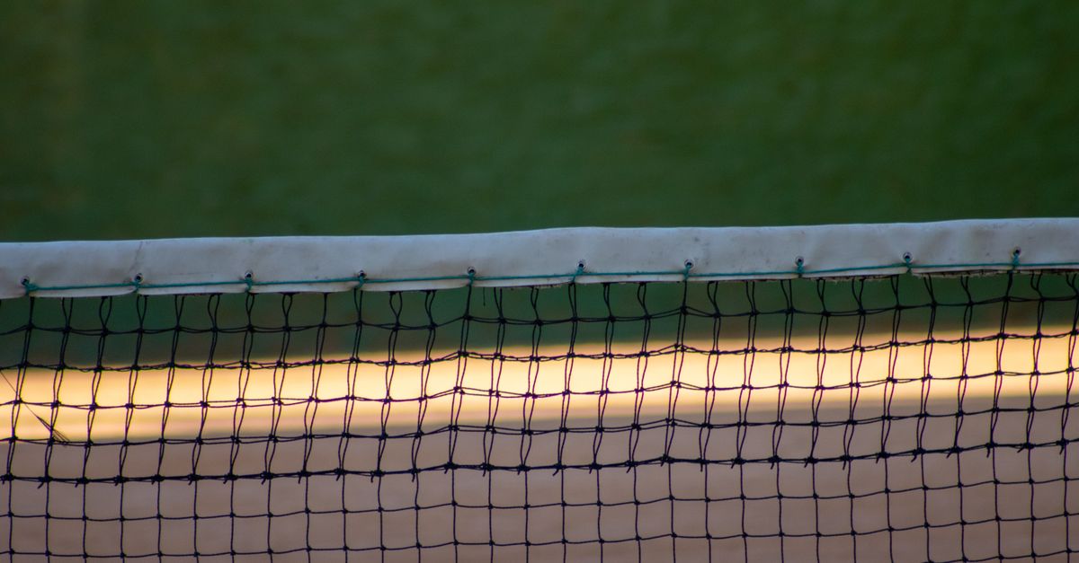 A detailed view of a tennis court net at dusk with a green court background, showcasing sports equipment.